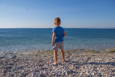 funny little boy jumping high on beach near sea shore in summer 