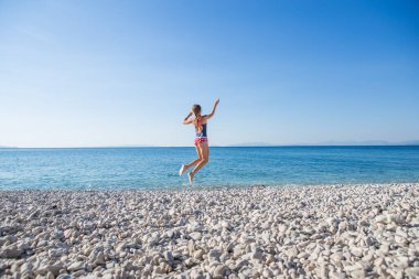 Genç sarışın kadın tatilde plajda zıplıyor.