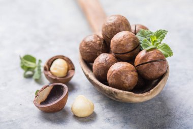 Macadamia fındıklarını istifleyin, çimento arka planda kaşık içinde çekirdekleri ve kabukları açın..