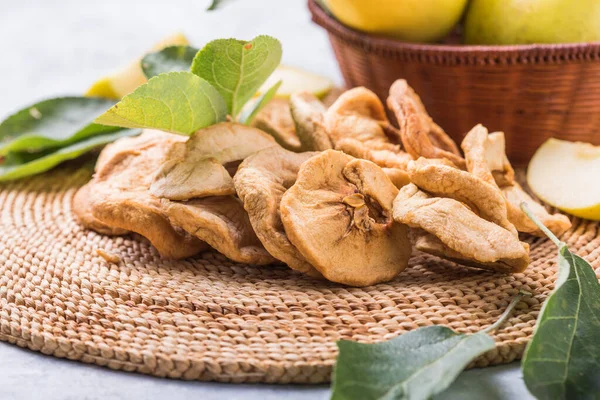 Dried apple chips and green fresh apples on a white table.