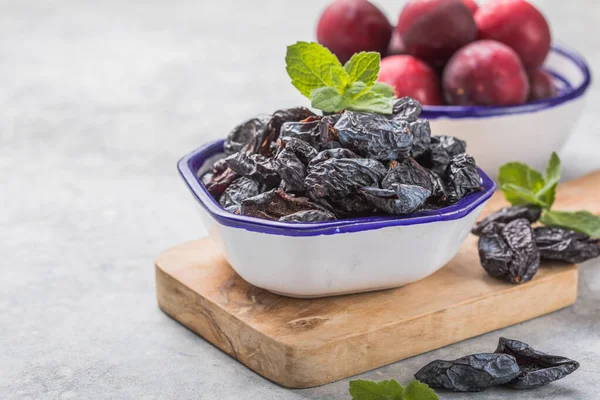 Dried plum or prunus in bowl with fresh plum fruits.