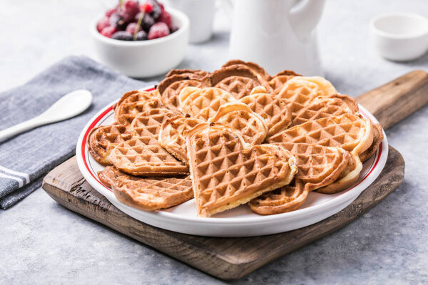 Freshly baked homemade heart shaped Belgium waffles  on gray background. European baked pastry sweets.  St. Valentine's Day breakfast concept.