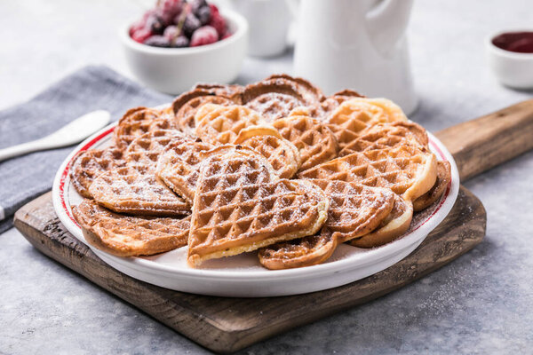 Freshly baked homemade heart shaped Belgium waffles  on gray background. European baked pastry sweets.  St. Valentine's Day breakfast concept.