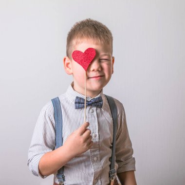 Beş yaşında gülümseyen bir çocuk, elinde aşkın, ailenin ve umudun sembolü olan kırmızı bir kalp tutuyor. Sevgililer Günü 'nde kart geçmişi ya da aile ve çocukların korunmasıyla ilgili sosyal afişler.