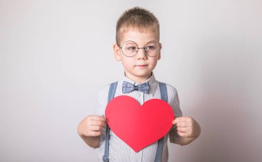Beş yaşındaki gülümseyen çocuk aşkın, ailenin ve umudun kırmızı kalp sembolünü taşıyor. Sevgililer Günü 'nde kart geçmişi ya da aile ve çocukların korunmasıyla ilgili sosyal afişler.