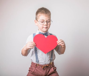 Beş yaşındaki gülümseyen çocuk aşkın, ailenin ve umudun kırmızı kalp sembolünü taşıyor. Sevgililer Günü 'nde kart geçmişi ya da aile ve çocukların korunmasıyla ilgili sosyal afişler.