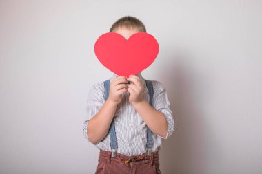 Beş yaşındaki gülümseyen çocuk aşkın, ailenin ve umudun kırmızı kalp sembolünü taşıyor. Sevgililer Günü 'nde kart geçmişi ya da aile ve çocukların korunmasıyla ilgili sosyal afişler.