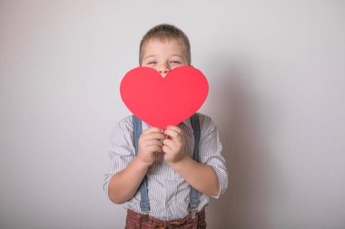 Beş yaşındaki gülümseyen çocuk aşkın, ailenin ve umudun kırmızı kalp sembolünü taşıyor. Sevgililer Günü 'nde kart geçmişi ya da aile ve çocukların korunmasıyla ilgili sosyal afişler.
