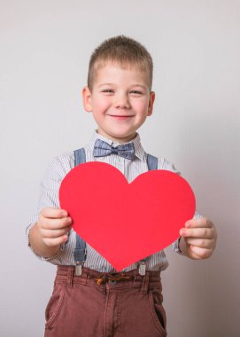 Beş yaşındaki gülümseyen çocuk aşkın, ailenin ve umudun kırmızı kalp sembolünü taşıyor. Sevgililer Günü 'nde kart geçmişi ya da aile ve çocukların korunmasıyla ilgili sosyal afişler.