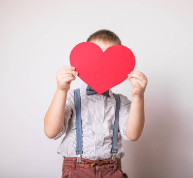 Beş yaşındaki gülümseyen çocuk aşkın, ailenin ve umudun kırmızı kalp sembolünü taşıyor. Sevgililer Günü 'nde kart geçmişi ya da aile ve çocukların korunmasıyla ilgili sosyal afişler.