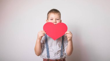 Beş yaşındaki gülümseyen çocuk aşkın, ailenin ve umudun kırmızı kalp sembolünü taşıyor. Sevgililer Günü 'nde kart geçmişi ya da aile ve çocukların korunmasıyla ilgili sosyal afişler.
