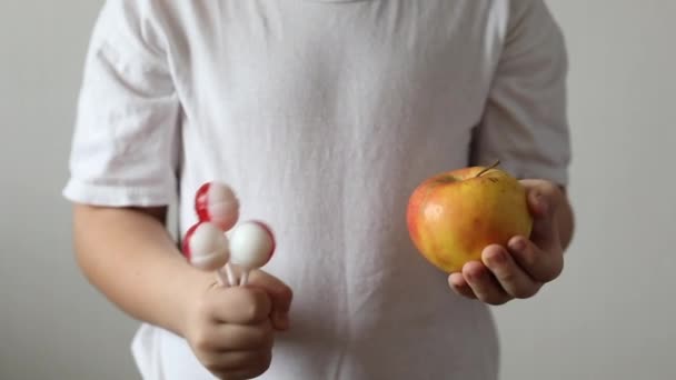 健康的で不健康な食品の概念 その少年は飴とりんごを持っている 彼女が食べたいものを選ぶ — ストック動画