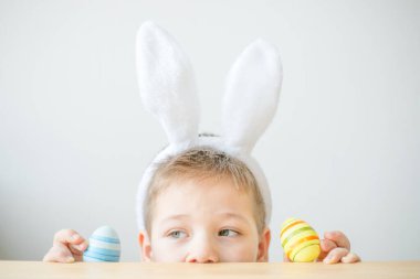 Tavşan kulaklı gülümseyen çocuğun portresi. Resim stüdyosunda, fotokopi odasında renkli yumurta tutuyor. Paskalya için hazırlanılıyor.