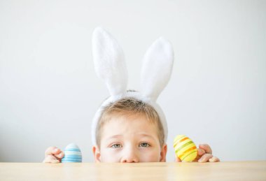 Tavşan kulaklı gülümseyen çocuğun portresi. Resim stüdyosunda, fotokopi odasında renkli yumurta tutuyor. Paskalya için hazırlanılıyor.