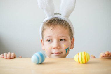 Tavşan kulaklı gülümseyen çocuğun portresi. Resim stüdyosunda, fotokopi odasında renkli yumurta tutuyor. Paskalya için hazırlanılıyor.