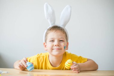 Tavşan kulaklı gülümseyen çocuğun portresi. Resim stüdyosunda, fotokopi odasında renkli yumurta tutuyor. Paskalya için hazırlanılıyor.