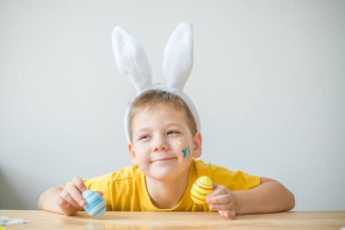 Tavşan kulaklı gülümseyen çocuğun portresi. Resim stüdyosunda, fotokopi odasında renkli yumurta tutuyor. Paskalya için hazırlanılıyor.