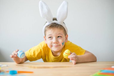 Tavşan kulaklı gülümseyen çocuğun portresi. Resim stüdyosunda, fotokopi odasında renkli yumurta tutuyor. Paskalya için hazırlanılıyor.