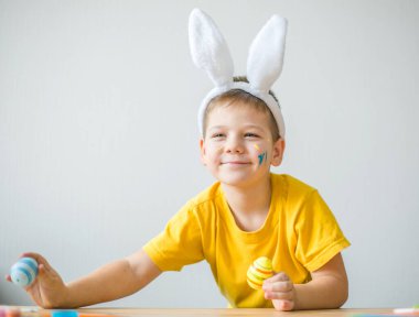 Tavşan kulaklı gülümseyen çocuğun portresi. Resim stüdyosunda, fotokopi odasında renkli yumurta tutuyor. Paskalya için hazırlanılıyor.