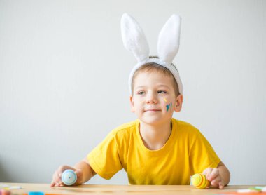 Tavşan kulaklı gülümseyen çocuğun portresi. Resim stüdyosunda, fotokopi odasında renkli yumurta tutuyor. Paskalya için hazırlanılıyor.