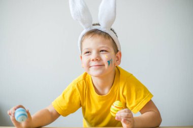 Tavşan kulaklı gülümseyen çocuğun portresi. Resim stüdyosunda, fotokopi odasında renkli yumurta tutuyor. Paskalya için hazırlanılıyor.