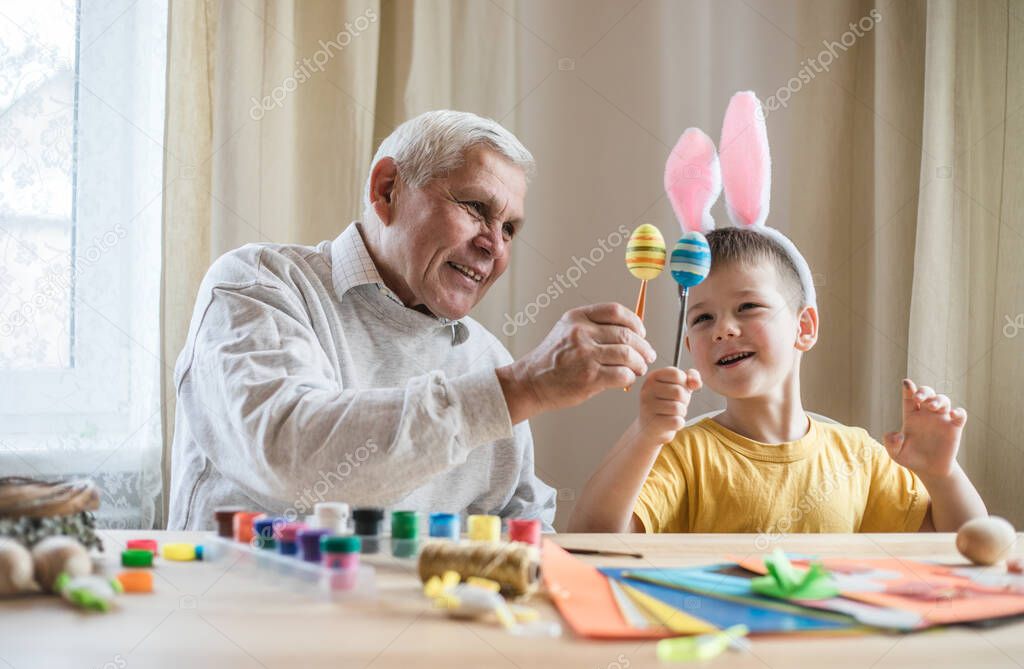 Happy elderly man granfather preparing for Easter with grandson. Portrait of smiling boy with bunny ears painted  colored eggs for Easter
