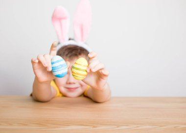 Paskalya günü tavşan kulağı takan şirin bir çocuk. Beyaz arka planda boyalı yumurta tutan çocuk..