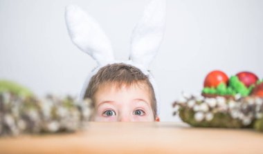 Paskalya günü tavşan kulağı takan şirin bir çocuk. Beyaz arka planda boyalı yumurta tutan çocuk..