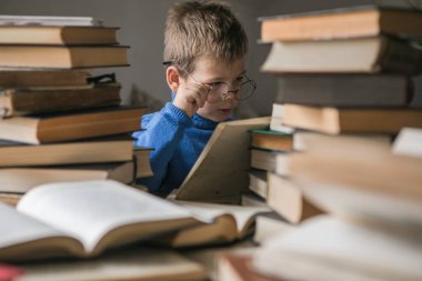 Beş yaşında gözlüklü bir çocuk yanında bir yığın kitapla kitap okuyor. Akıllı akıllı anaokulu çocuğu ödünç kitap seçiyor..