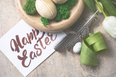 Paskalya kompozisyonu ahşap Paskalya yumurtaları ve bahar çiçekli laleler beton arka planda. Paskalya kartını kapat.