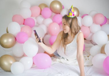 Neşeli bir kadının gülümsemesi ve cep telefonuyla balonla selfie çektiği fotoğraf. Doğum günü partisi