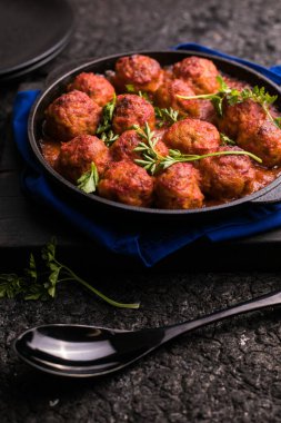 Meat balls with tomato sauce  in a frying pan on a black background.