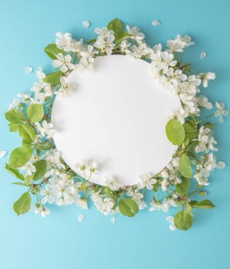 Zarif bir çiçek kompozisyonu ve mavi arka planda boş kağıt var. Marka modeli, tatil pazarlama konsepti. Kiraz ve beyaz çiçeklerin bileşimi çerçeve etrafında sıralanmıştır. Tebrik kartı şablonu. Mutlu kadınlar günü, bahar, eas