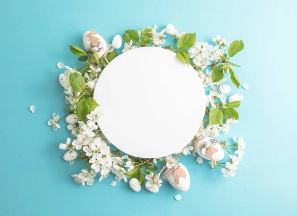 Easter  floral, eggs, composition with paper round blank in the centre of blue background. Branding mock up, holiday marketing concept. Composition of cherry and white flowers is lined with frame around. Greeting card template. Happy womans day, spri