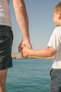 Küçük çocuk babasının elini tutuyor. Genç adam, kumsalda yürüyen küçük çocuk babalar günü. Babanızla mutlu bir çocukluk.