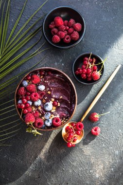 Hindistan cevizi kabuklu donmuş acai smoothie ahududu, muz, yaban mersini, meyve ve granola ile beton arka planda. Kahvaltı, yaz havası için sağlıklı yemek, üst manzara, yazı için yer