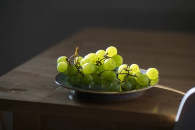 Taze yeşil üzümler, arka planda ışıklandırılmış, desen ve tazelik vurgulanıyor.