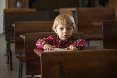 Kaliteli sınıfta, eski tahta bir masada açık bir kitapla oturan genç bir çocuk.
