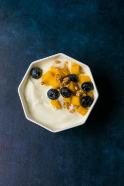 Sağlıklı yoğurt, mango yaban mersinli meyve suyu kasesi ve granola, kahvaltı için mükemmel ya da hafif bir tatlı..