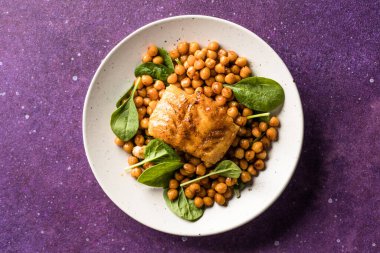 Tavada kurutulmuş morina balığı, bezelye ve beyaz tabakta taze ıspanakla servis edilir.