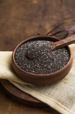 Koyu bir arka planda, ahşap bir kasede servis edilen doğal chia tohumları.