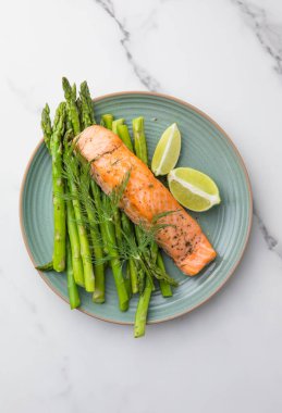 Kavrulmuş kuşkonmaz ve mevsimlik sebzelerle servis edilen sağlıklı pişmiş somon. Temiz yemek, dengeli beslenme, ev yemeği konsepti..