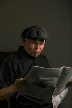 Siyah şapka ve gömlek giyen yaşlı bir adamın yakın plan, sade bir portresi. Nazik ve düşünceli bir ifadeyle hafifçe yukarı bakıyor. Yumuşak ışık yüzündeki kırışıklıkları vurguluyor, karamsar ve iç gözlemci bir atmosfer yaratıyor..