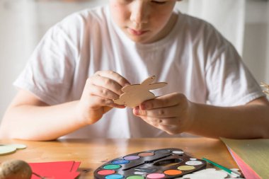 Küçük çocuk evde ahşap Paskalya tavşanı çiziyor.