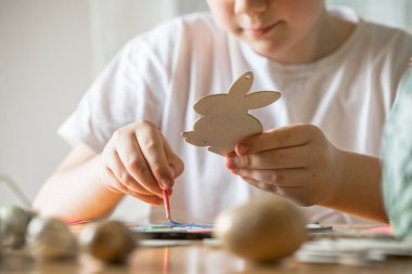 Küçük çocuk evde ahşap Paskalya tavşanı çiziyor.