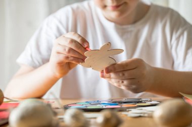 Küçük çocuk evde ahşap Paskalya tavşanı çiziyor.