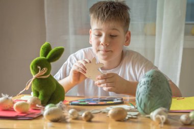 Küçük çocuk evde ahşap Paskalya tavşanı çiziyor.