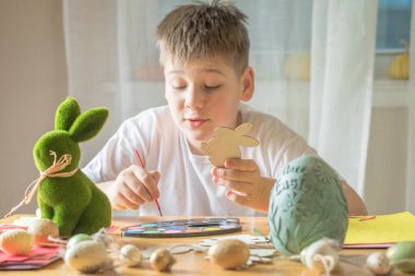 Küçük çocuk evde ahşap Paskalya tavşanı çiziyor.