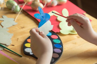 Küçük çocuk evde ahşap Paskalya tavşanı çiziyor.