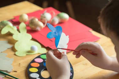 Küçük çocuk evde ahşap Paskalya tavşanı çiziyor.